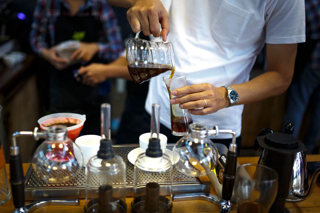 who-we-are A barista carefully pouring brewed coffee into a clear glass in a coffee shop.