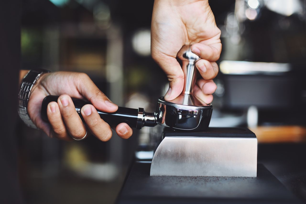about-hero Close-up of a barista tamping coffee grounds using an espresso tamper.