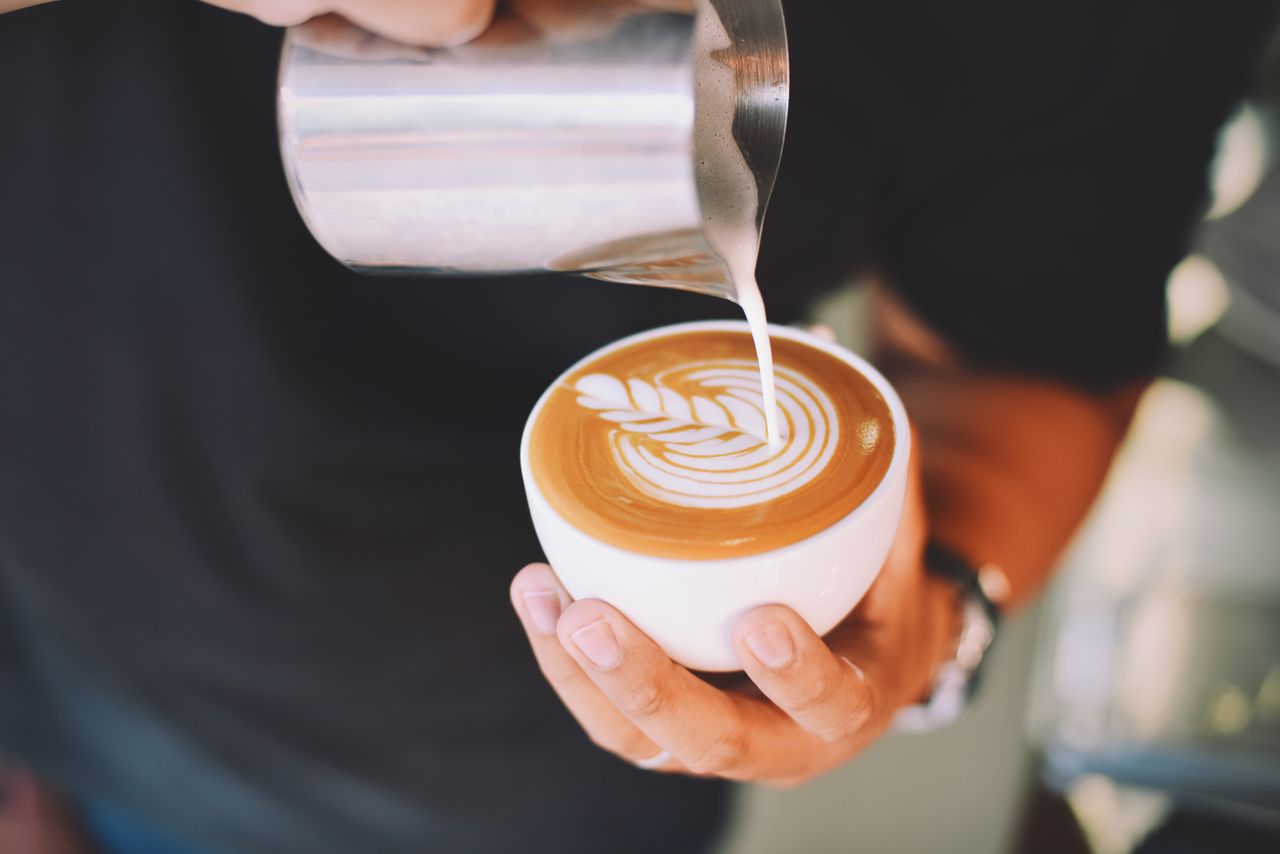 about-02 Close-up of a barista pouring latte art into a coffee cup indoors.