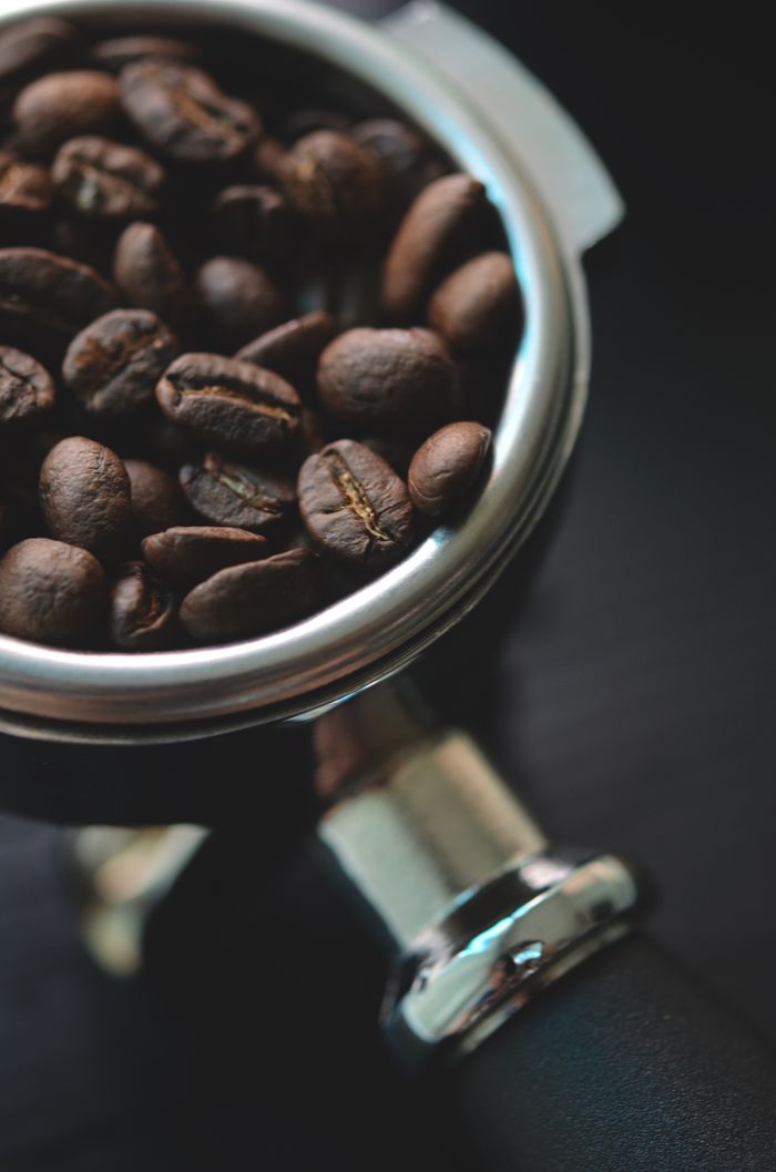 why-choose-us Aromatic coffee beans resting in a metal portafilter, ready for brewing.
