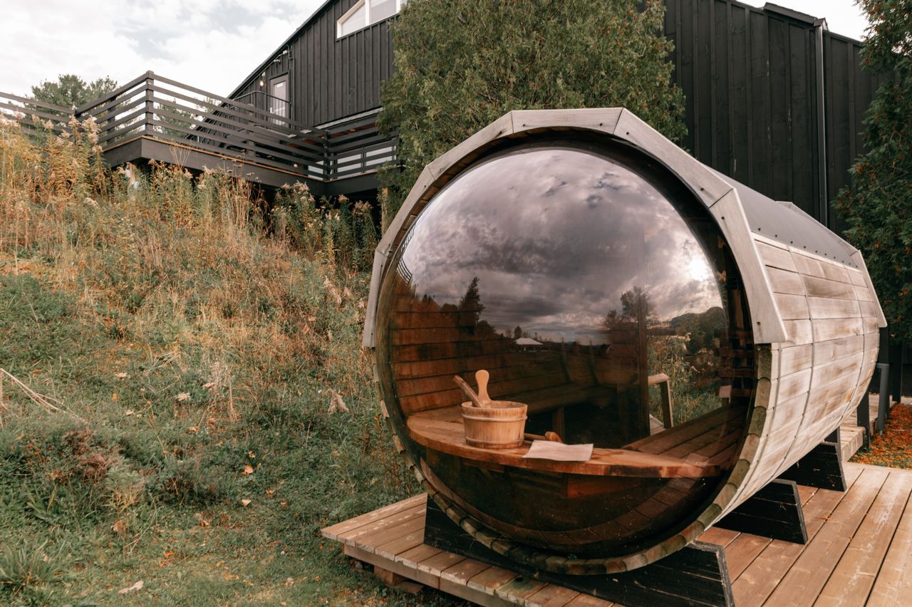 Rustic barrel sauna with glass front set in natural landscape, perfect for relaxation.
