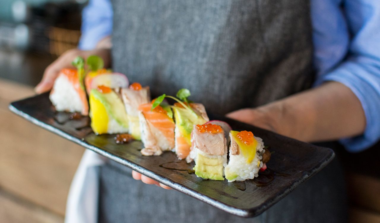 Home Colorful sushi rolls with salmon, avocado, and roe served on a ceramic plate by a chef in a restaurant.