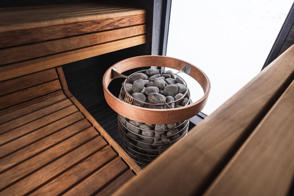 A cozy modern sauna with a wooden interior and a central heater with stones, ready for relaxation.