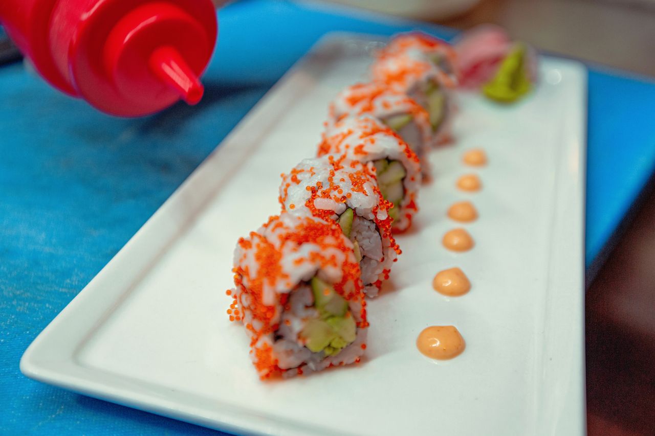 about-img Close-up of fresh sushi rolls topped with roe, served with wasabi and sauce dots on a plate.